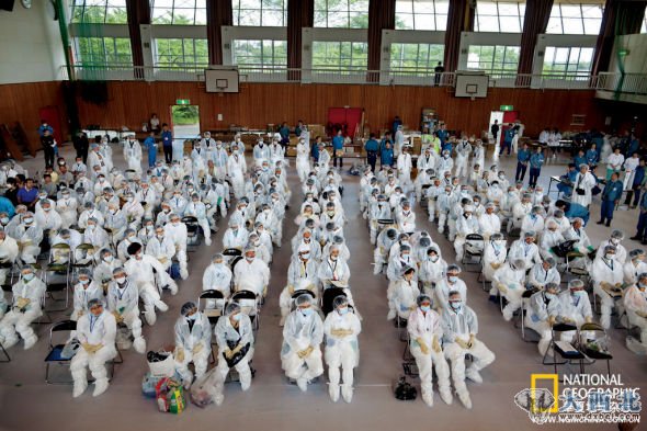 6月8日，广野町的一个体育馆里，身穿防护服的居民正听人们向他们介绍注意事项，之后他们将在专人护送之下回到家中，取回几样小物品。（巴士上没有搁置大件物品的空间。）一名当地官员称，尽管来的路上戒备森严，但在排除污染的过程中（处理鞋套、防护服、帽子和口罩，并对人们进行放射物排查），所有人和物品都被放了一马。